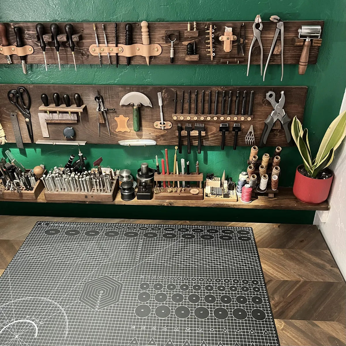 Direct view of a clean cutting mat station backed by custom leathercraft tool racks and potted studio greenery in Miami Beach.