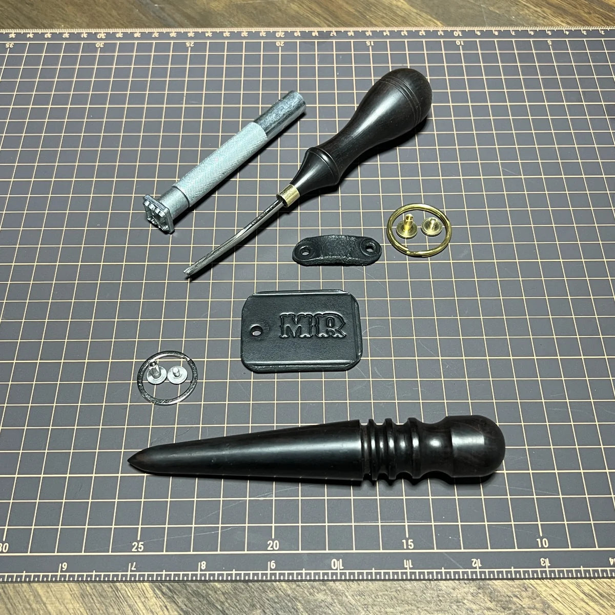 Component detail layout displaying 3D "MR" metal monogram stamp, edge slicker burnishing tool, solid brass Chicago screw, and leather keeper loop at Deco Leather Studio.