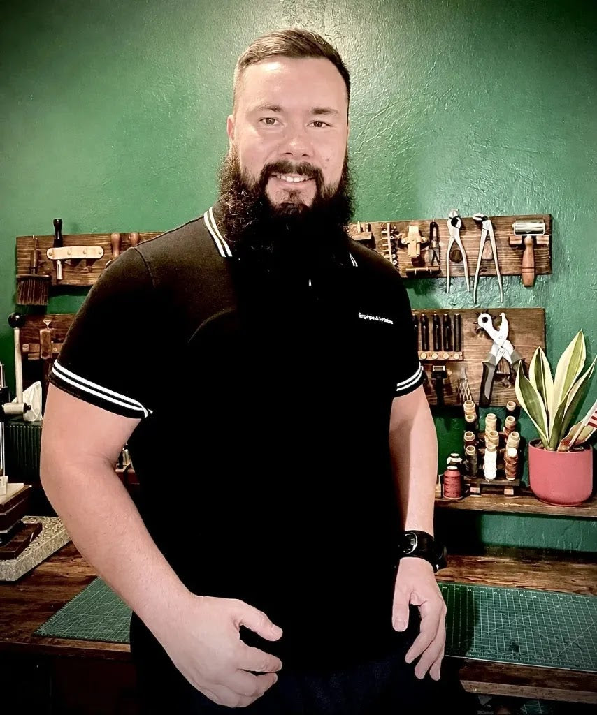 Portrait of leather artisan smiling in front of a wood-mounted hand tool rack and leathercraft workbench inside Deco Leather Studio in Miami Beach.