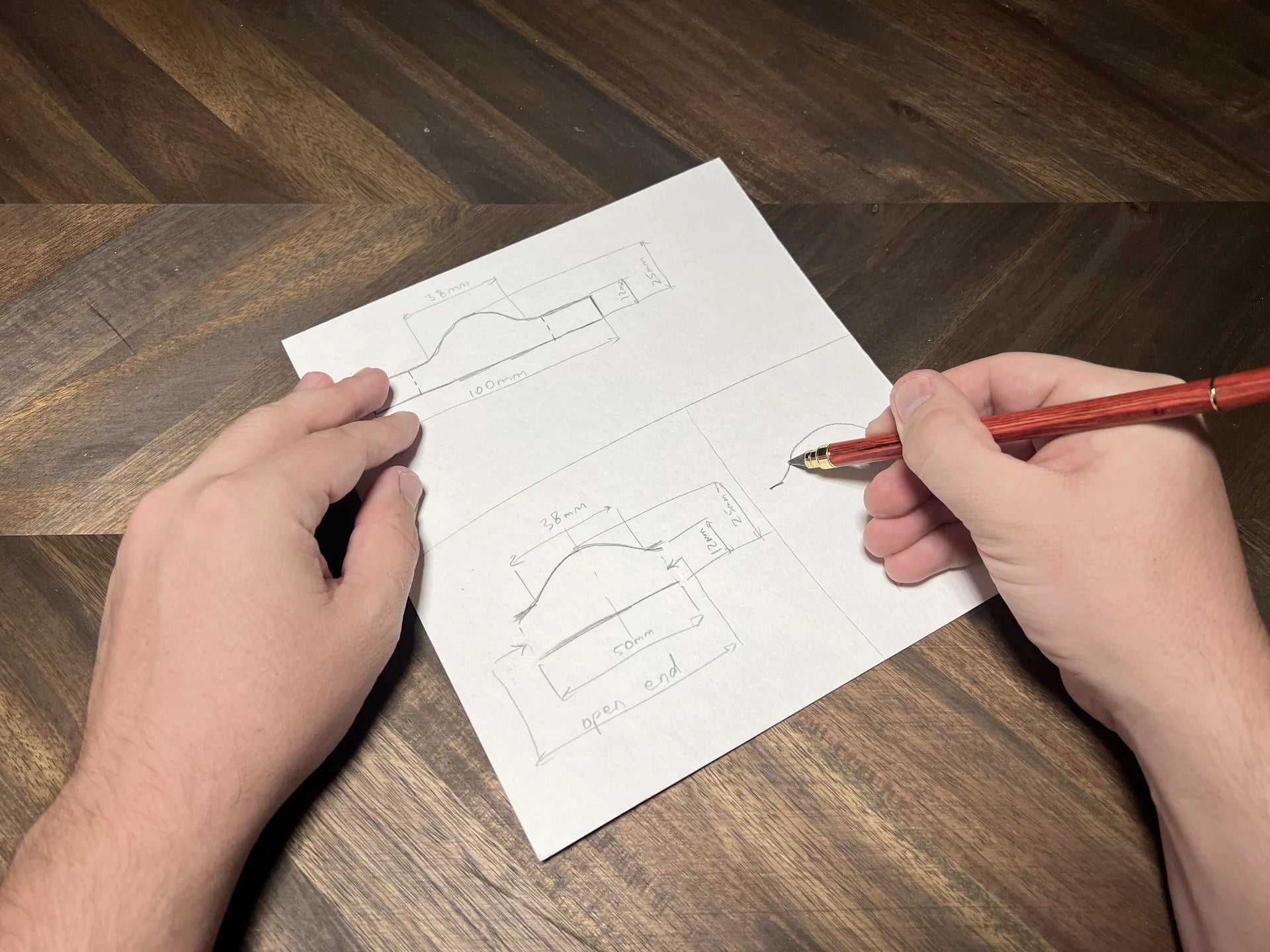 Top-down view of artisan hands drawing custom leather product templates and curves with exact dimension markings on a chevron wood work table at Deco Leather Studio.