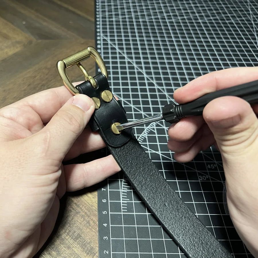 Close-up view of artisan installing brass Chicago screws on a black leather strap using a precision screwdriver at Deco Leather Studio in Miami Beach.