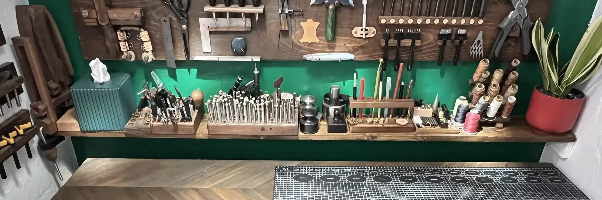 The Deco Leather Studio workbench in Miami Beach, with wall-mounted leatherworking tool boards, punches, stamps, and thread above the work surface.