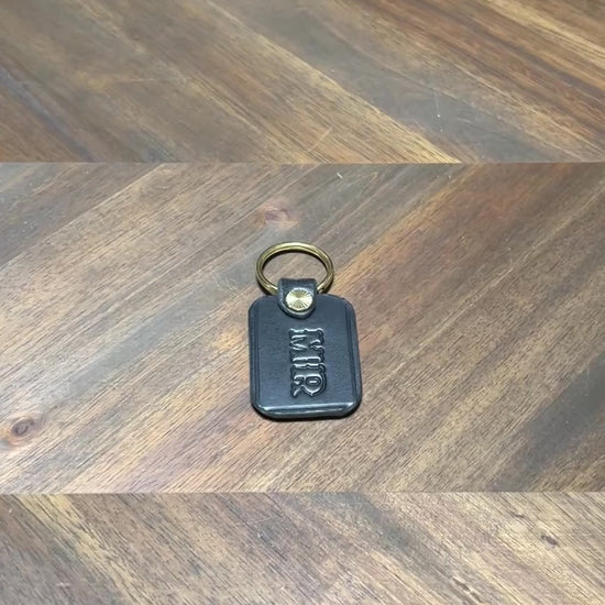 Silent 1080p hands-on video inspection highlighting the burnished edges, custom monogramming, and brass split ring of the handcrafted black leather key fob.